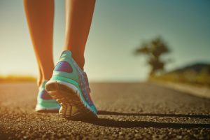 Closeup of female runner shaved feet in running shoes going for a run on the road at sunrise or sunset. Shallow depth of field, toned with instagram like filter, flare effect.